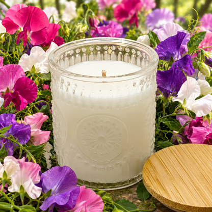 soy candle in a clear embossed glass jar surrounded by sweet peas